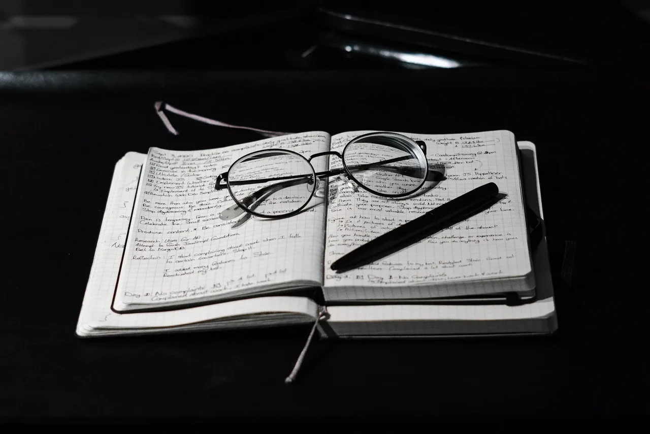 Un carnet de notes manuscrites, des lunettes et un stylo posés sur un bureau.