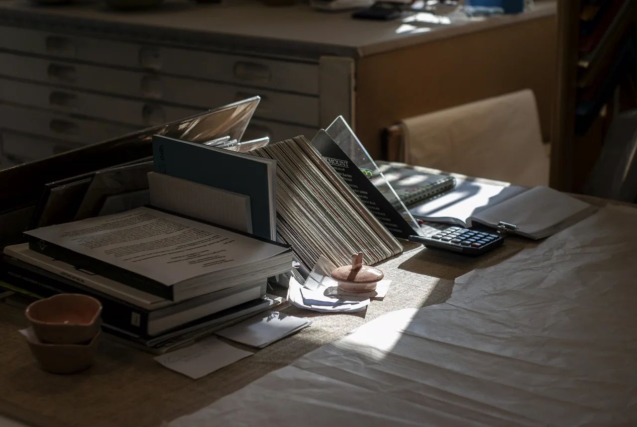 Des dossiers, des documents et une calculatrice sur un bureau, dans la lumière du jour.